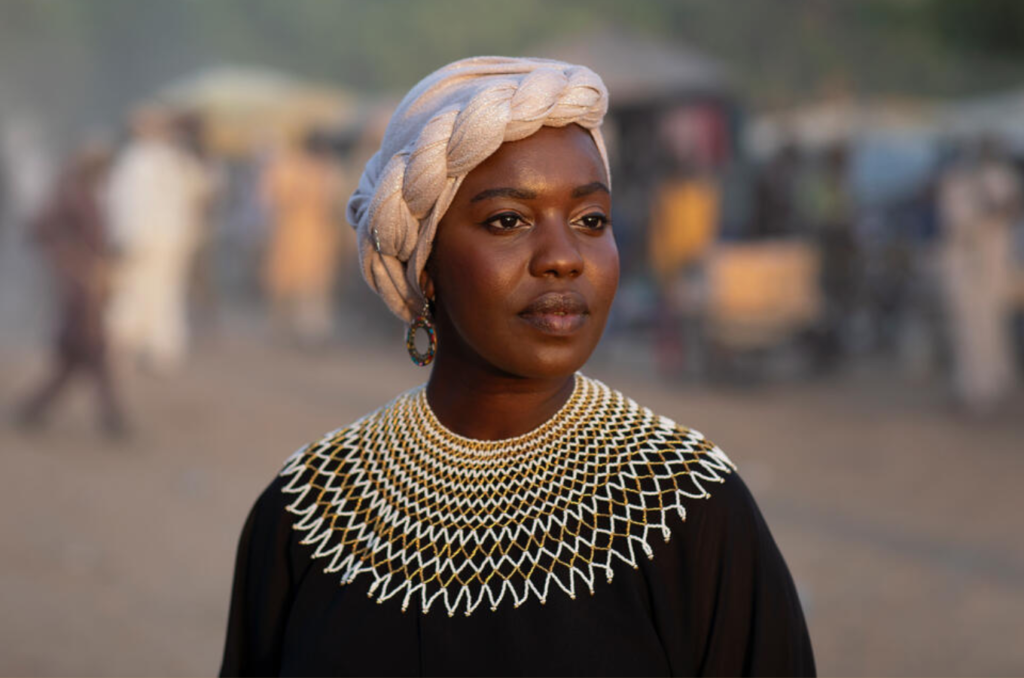 A woman in an overflowing black dress with knitted thread around her neck.